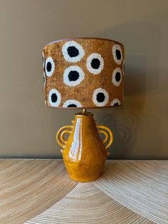 a yellow vase sitting on top of a wooden table next to a brown lamp shade