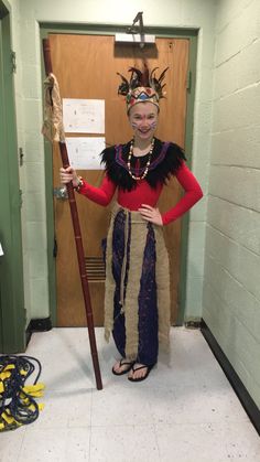 a woman dressed in costume holding a stick and wearing a feathered headdress