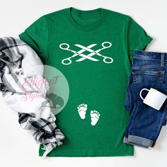 a green t - shirt with scissors on it next to some jeans and a mug