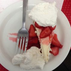 a white plate topped with strawberries and whipped cream next to a fork on top of a table