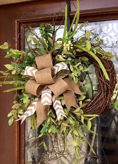 a wreath hanging on the front door decorated with greenery and burlap bows