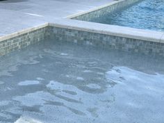 an empty swimming pool next to a tiled wall and water feature in the back yard