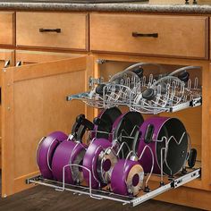 an open dish rack with purple pots and pans in the bottom drawer on a wooden kitchen countertop