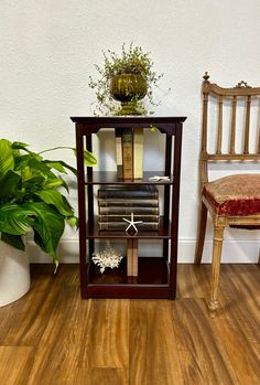 a wooden shelf with books on top of it next to a chair and potted plant