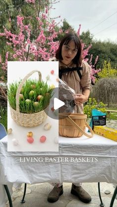 a woman standing in front of a table holding a basket filled with grass and eggs