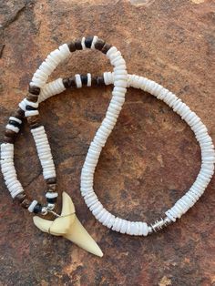 two necklaces with white and brown beads are on top of a rock, next to a bone