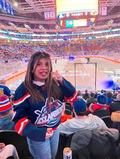 a woman standing in front of an ice hockey rink giving the thumbs up sign while people watch