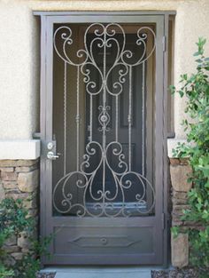 an iron door is shown in front of some bushes and plants on the side of a house