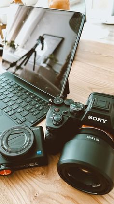 a laptop computer sitting on top of a wooden table next to a camera and lens