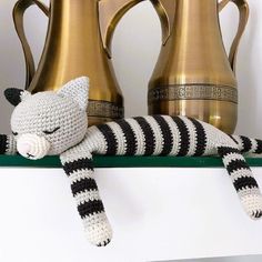 a crocheted cat laying on top of a shelf next to two vases