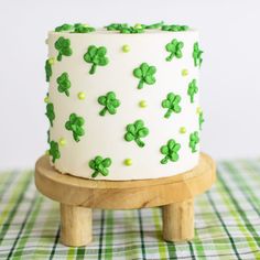 a white cake with green shamrocks on it sitting on top of a wooden stand