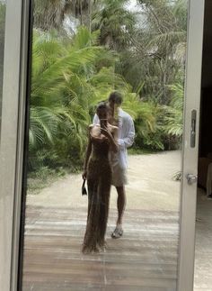 a man and woman standing in front of a glass door with palm trees behind them