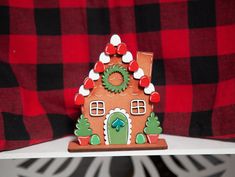 a gingerbread house with a wreath on the top and red checkered curtains behind it