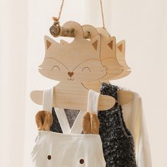 a wooden cat decoration hanging on a wall next to a pair of overalls with suspenders