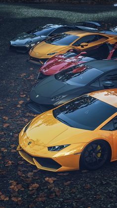 several different colored sports cars are parked in a parking lot with leaves on the ground