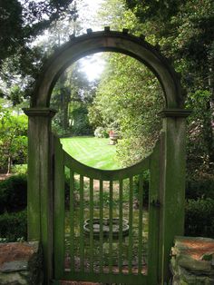 an arched wooden gate in the middle of a lush green park