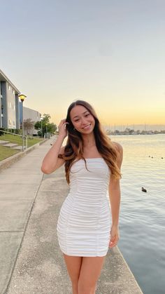 a woman in a short white dress is standing on the edge of a pier and smiling