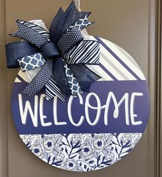 a blue and white welcome sign hanging on the front door with ribbon attached to it