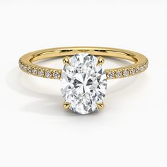 a yellow gold engagement ring with an oval cut diamond in the center and pave set shoulders