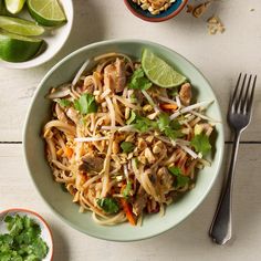 a white bowl filled with noodles and vegetables next to two bowls of limes, nuts and cilantro