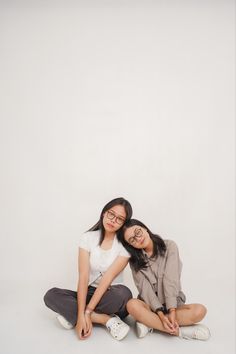 two young women sitting on the ground posing for a photo together with their arms around each other