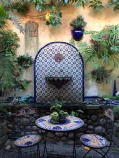 an outdoor table and chairs in front of a wall with potted plants on it