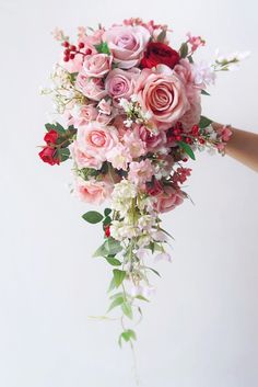 a bouquet of pink and red flowers is being held by a woman's hand