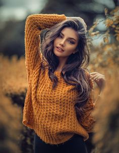 a beautiful young woman posing with her hands on her head and wearing a yellow sweater