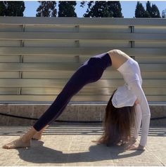 a woman in white shirt and black pants doing a handstand on the ground