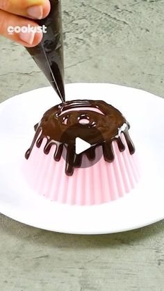 someone is decorating a chocolate donut on a white plate with pink and black icing