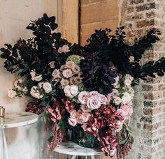 an arrangement of flowers in a vase on a table next to a brick wall and chair