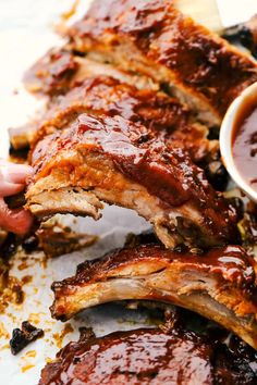 ribs with barbecue sauce being held up by someone's hand and dipping them into a small bowl