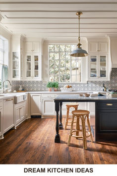 a kitchen with wooden floors and white cabinets, an island countertop and stools