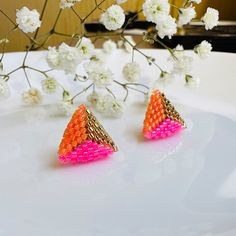 two pink and orange earrings sitting on top of a white plate next to some flowers