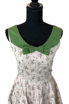 Romance is back! Elizabeth in Antique Floral is the dreamy dress you need in your wardrobe! Sleeveless, with an old fashioned floral print in seersucker, this beauty features a split peter pan color in green cotton and an adorable detachable bow to accent the collar or waistline. The dress comes with a matching green bow that is a removable pin. There are two placements we recommend in the photos - either at the collar or waistline. Play around and see what you like best! Elizabeth is perfect fo Cotton Dress With Peter Pan Collar For Summer, Cotton Summer Dress With Peter Pan Collar, Green Floral Print Dresses For Picnics, Green Floral Print Dresses For Picnic, Green Floral Print Dress For Picnic, Cottagecore Green Cotton Dress, Green Cotton Cottagecore Dress, Summer Green Vintage Dress With Ruffles, Green Cotton Dress For Picnic