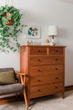 a wooden dresser sitting next to a chair and potted plant on top of it