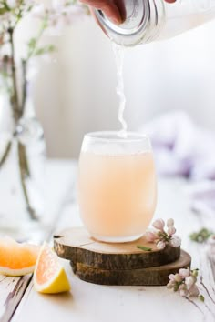 a glass filled with liquid sitting on top of a wooden table next to sliced lemons