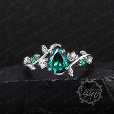 an emerald colored ring with leaves and vines on the side, sitting on a black surface