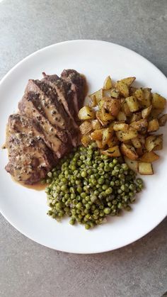 a white plate topped with meat, potatoes and peas