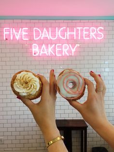 two hands holding doughnuts in front of a neon sign that says five daughters bakery