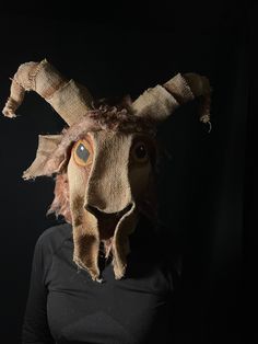 a person wearing a goat mask with long hair and big eyes in front of a black background