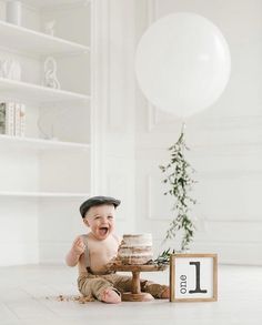 a baby boy sitting on the floor with his first birthday cake in front of him