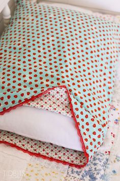 a bed with blue and red polka dot sheets on it's sides, along with white pillows