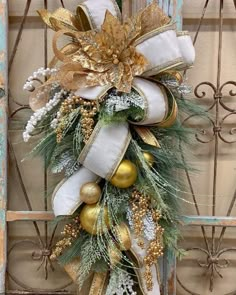 a christmas wreath with gold and white decorations on it, hanging in front of a door