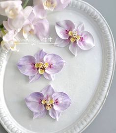 three purple flowers sitting on top of a white plate next to some pink and yellow flowers