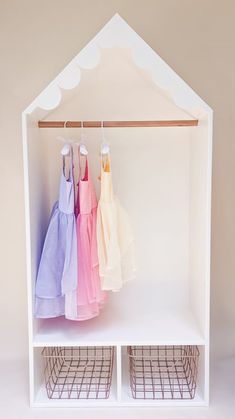 three dresses are hanging on the rack in front of a white shelf with wire baskets