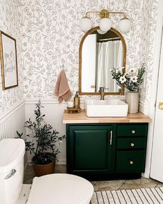 a white toilet sitting next to a green cabinet in a bathroom under a large mirror