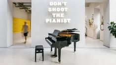 a black piano sitting in the middle of a room next to a sign that says don't shoot the pianist