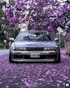 a car is parked on the side of the road with purple flowers all over it