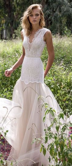 a woman in a wedding dress is walking through the grass with her hand on her hip